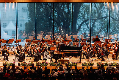 das Orchester des Tiroler Landeskonservatoriums spielt live auf einer Konzertbühne mit Publikum in den ersten Reihen