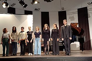 8 Personen (Studierende und Lehrende) stehen auf der Bühne