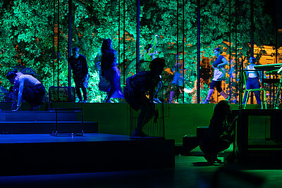 Studierende in bunten Kostümen performen live auf der Bühne