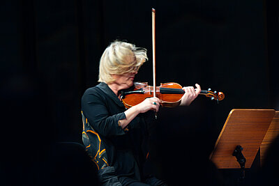Eine Muikerin spielt live im Scheinwerferlicht auf einer dunklen Konzertbühne Violine. 