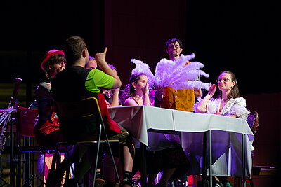 Studierende in bunten Kostümen performen live auf der Bühne 
