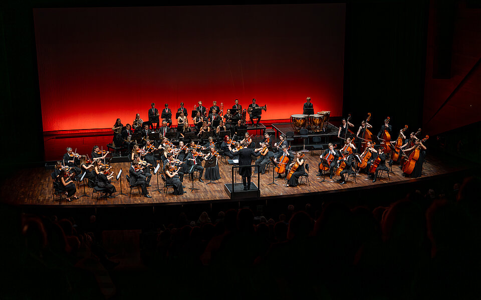 Orchester auf einer modernen Konzertbühne im roten Scheinwerferlicht