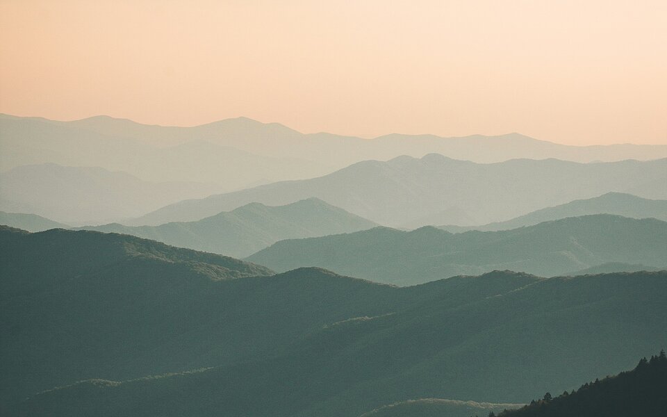 Landschaft mit nach hinten unscharf verlaufenden Bergen und rosa Himmel