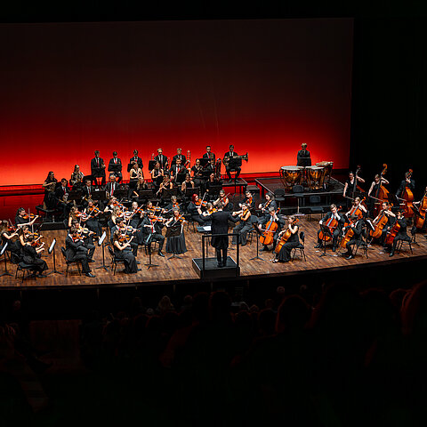 Orchester auf einer modernen Konzertbühne im roten Scheinwerferlicht