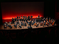 Orchester auf einer modernen Konzertbühne im roten Scheinwerferlicht