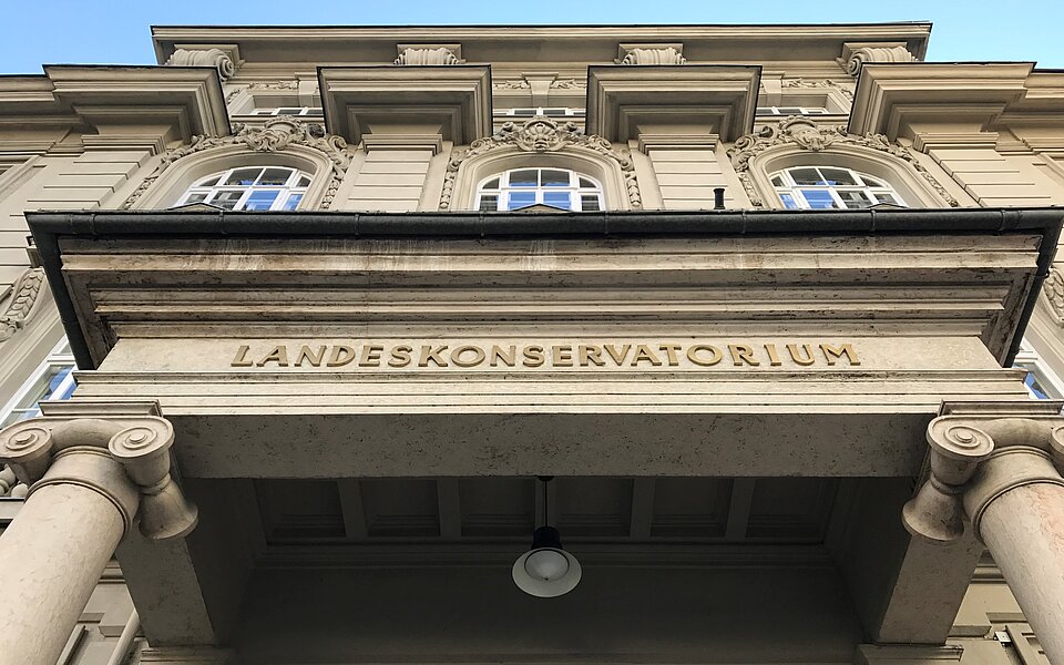 Fasade des Tiroler Landeskonservatoriums mit Schriftzug nach oben fotografiert, blauer Himmel im Hintergrund